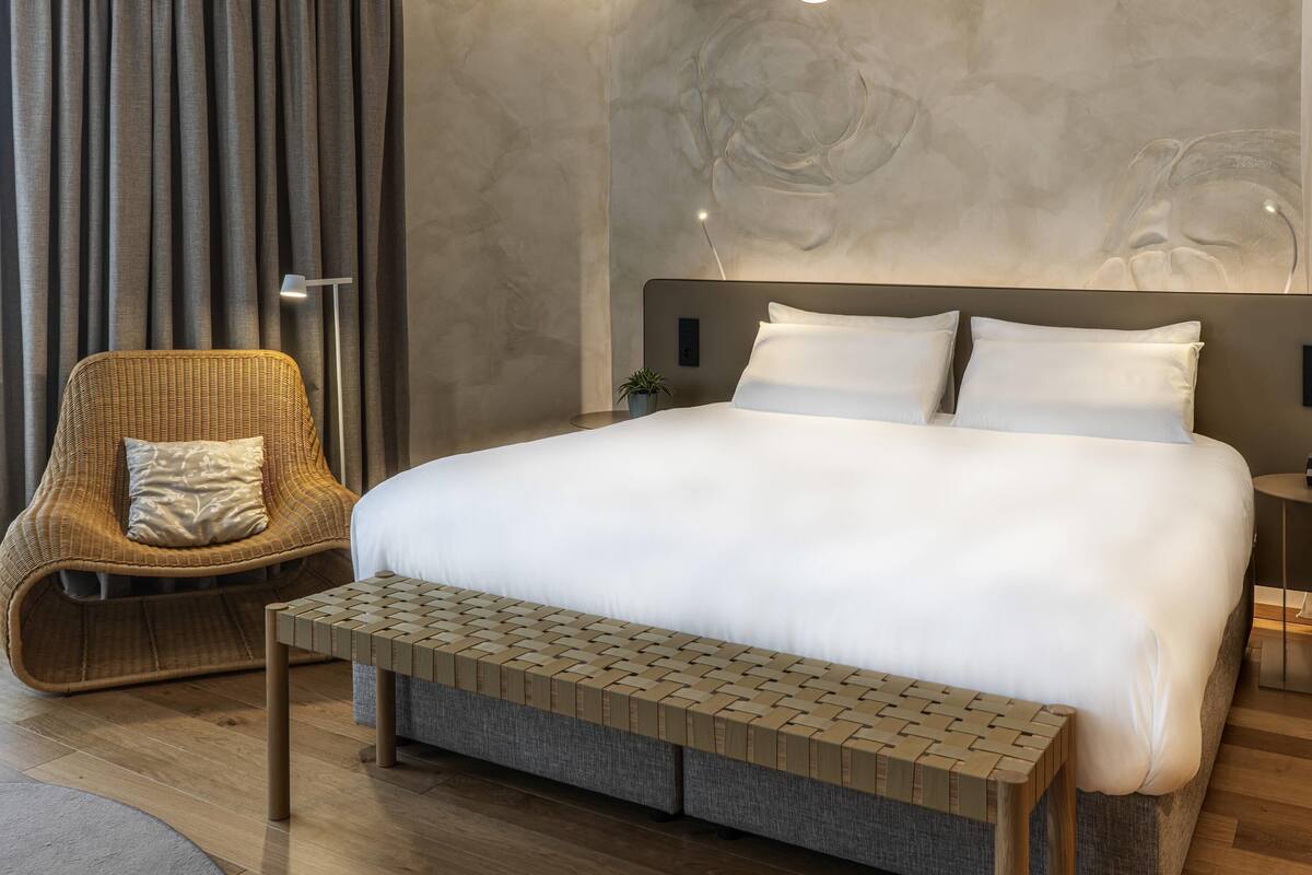 Een moderne hotelkamer met een groot bed, een rieten stoel, een klein tafeltje en een wandlamp.