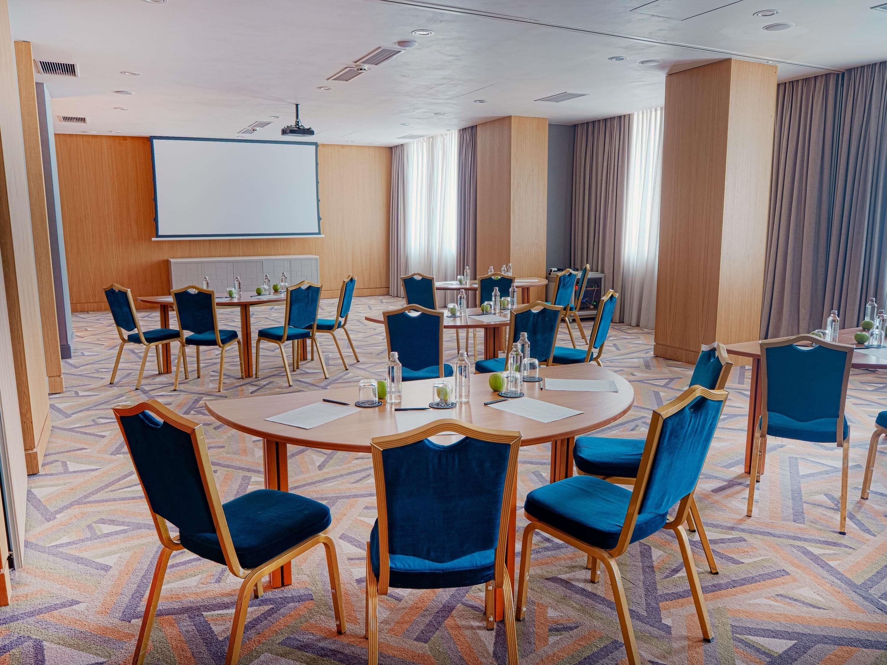 A conference room with round tables, blue upholstered chairs, and a whiteboard.