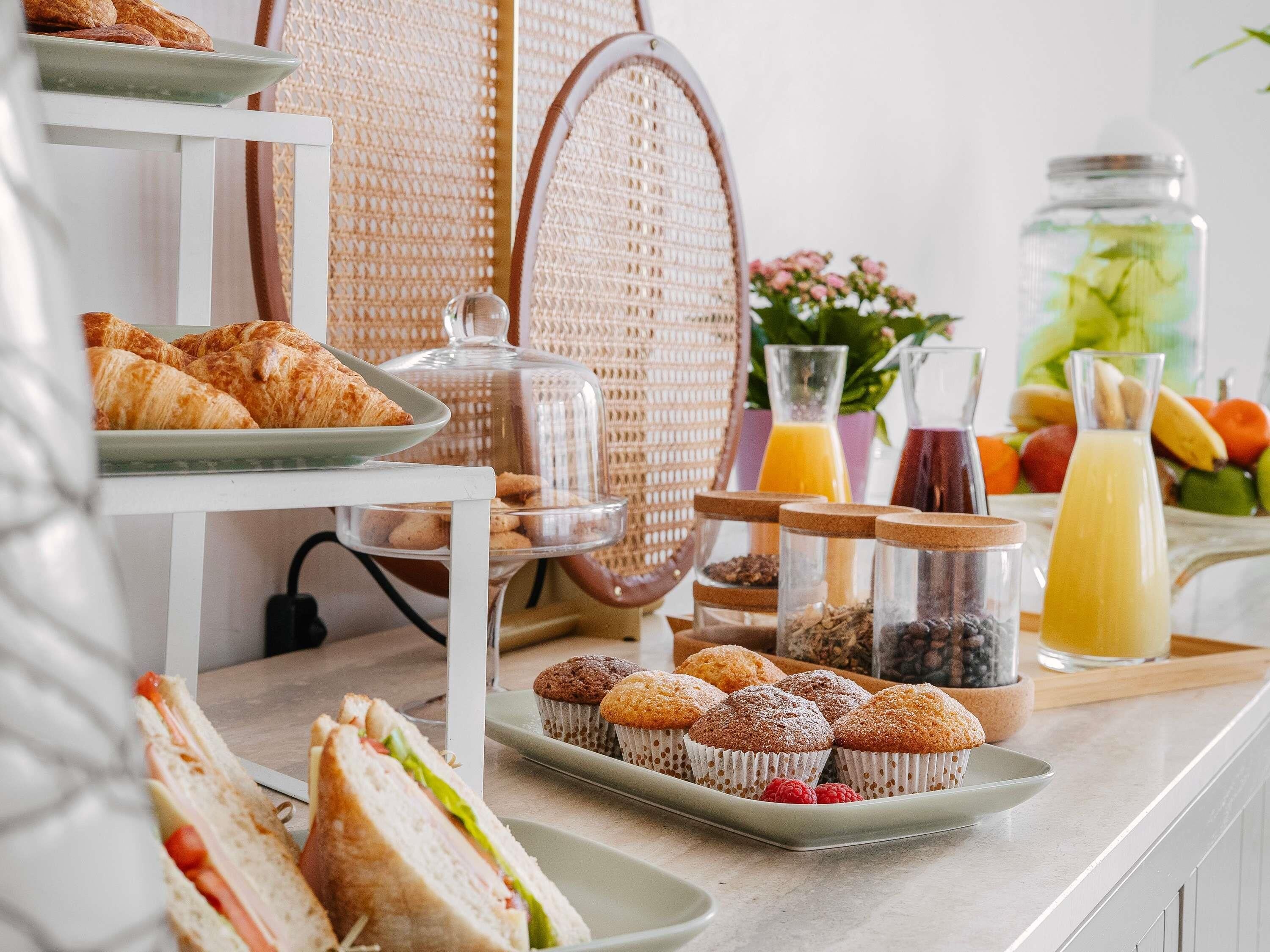 A breakfast buffet with pastries, muffins, and sandwiches.