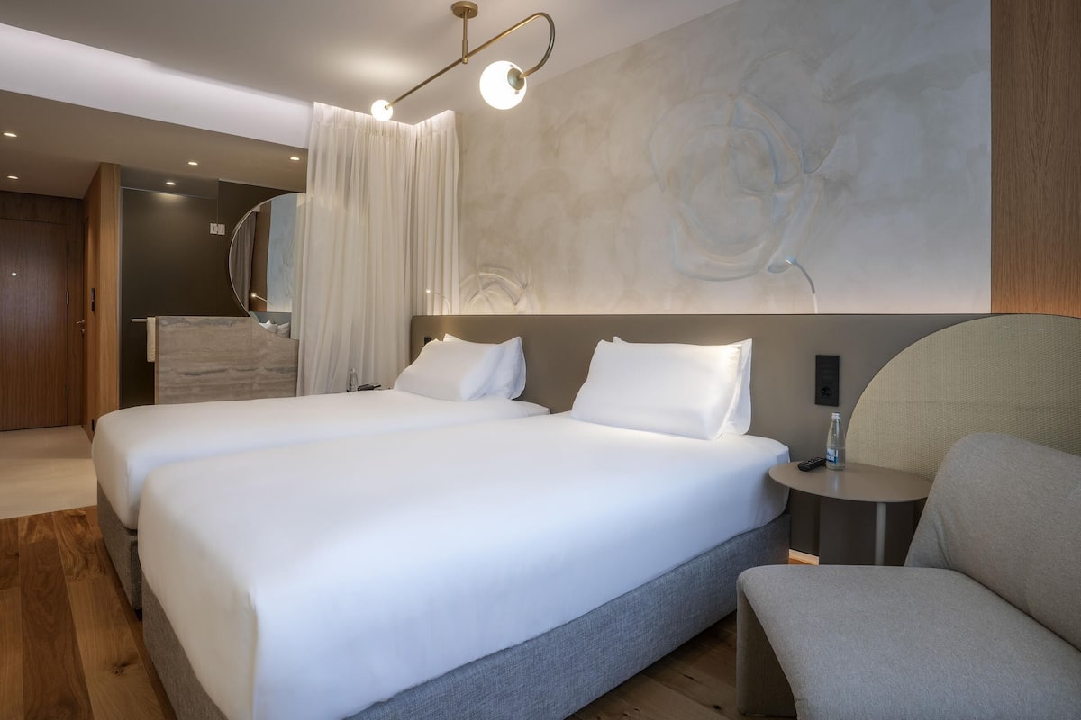 A double bed with a grey headboard, a bedside table with a lamp, and a large abstract wall painting.