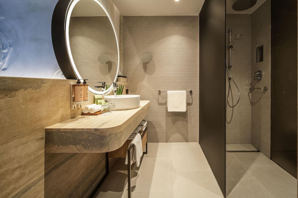 A modern bathroom with a large mirror, a sink, a towel rack, and a shower area.