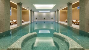 En moderne indendørs swimmingpool med krystalklart vand, liggestole og plantekasser.