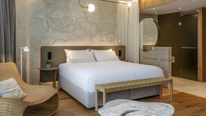 Una habitación de hotel moderna con una cama grande, una mesita de noche, una silla y una mesa de centro con diseño de mármol.