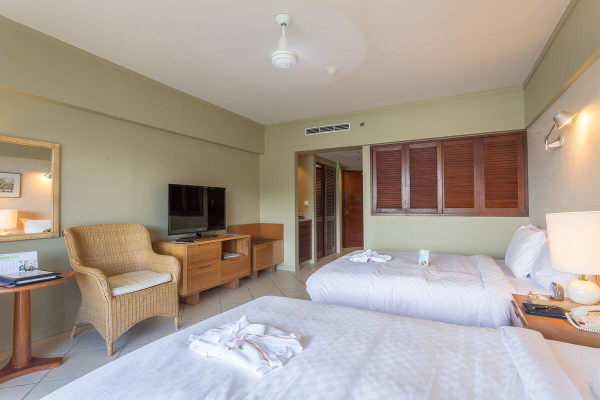 Une chambre d’hôtel avec deux lits, une télévision, un bureau, une chaise et une armoire.