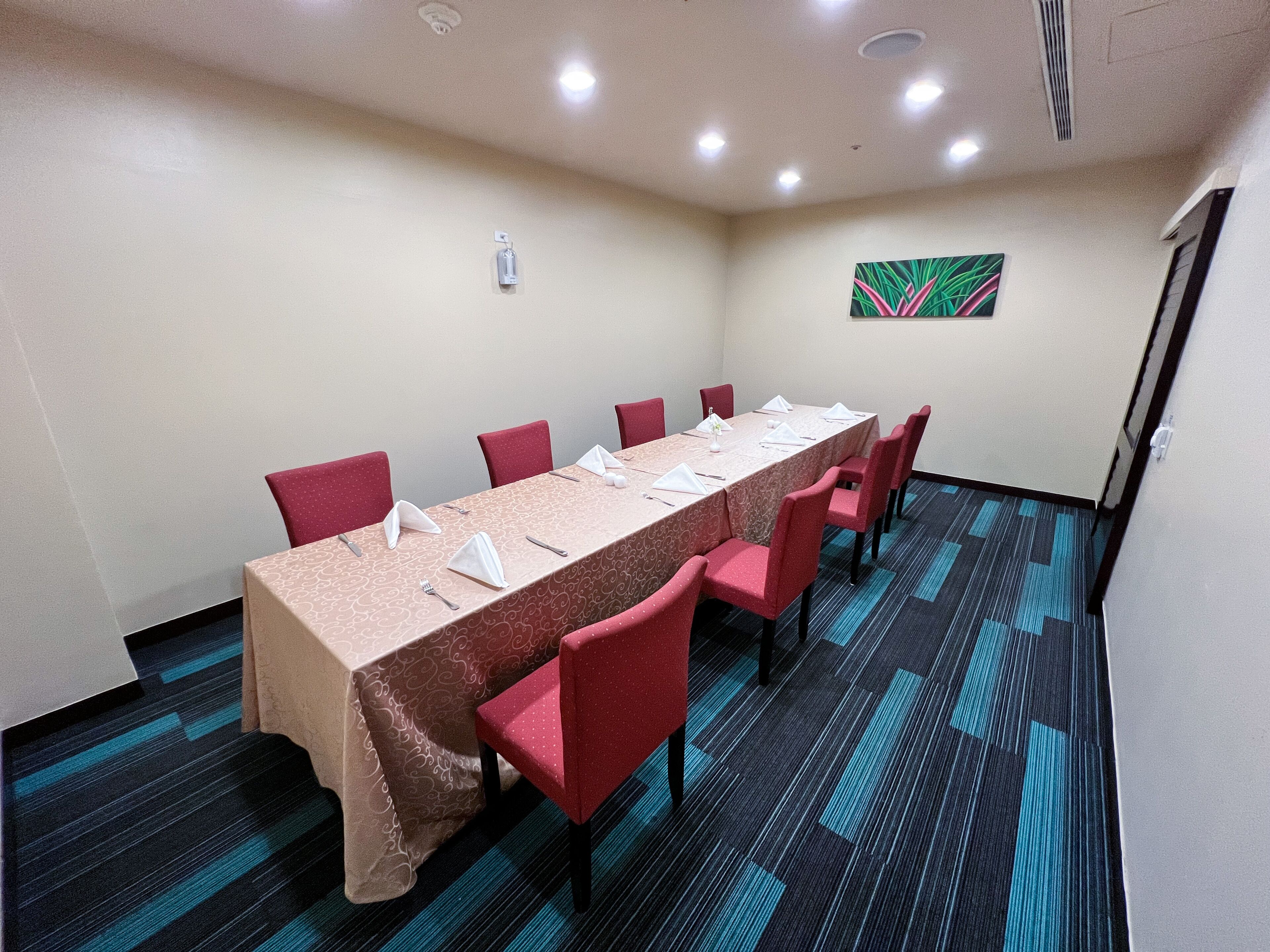 A conference room with a long table, red chairs, and a patterned carpet.