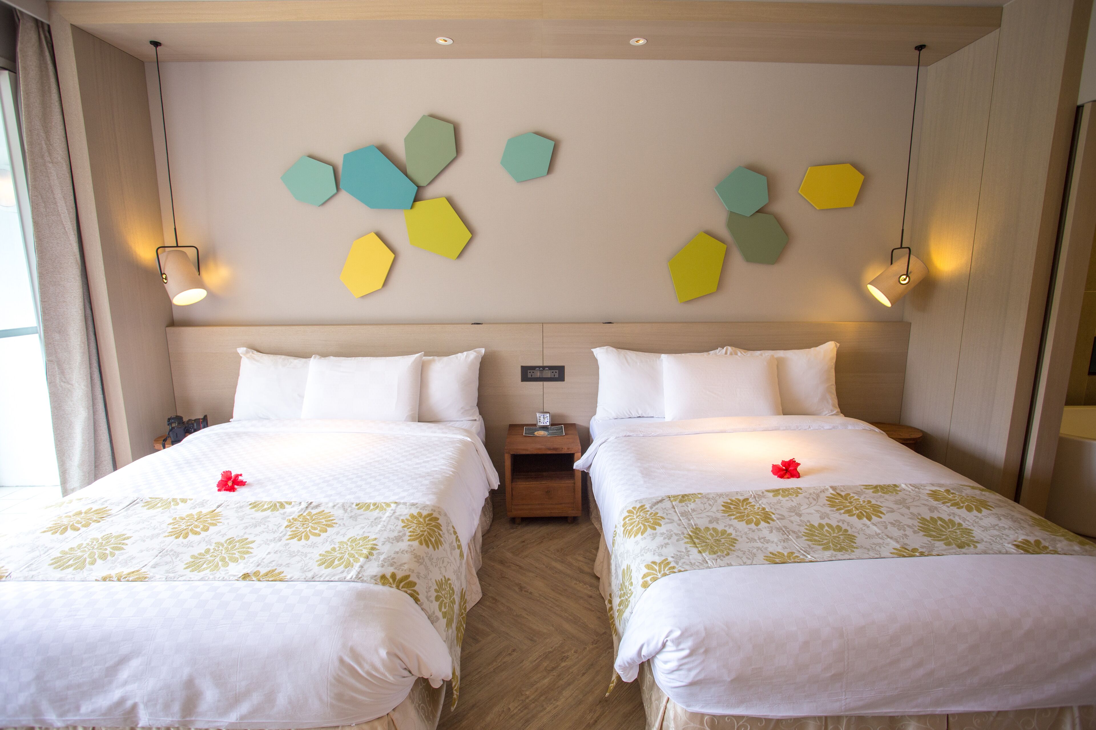 A hotel room with two beds, a wooden floor, and a wall with hexagonal wall art.