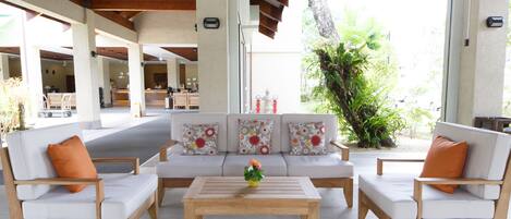 A spacious outdoor seating area with a wooden coffee table and white cushioned sofas with orange pillows.