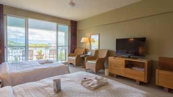 A hotel room with two beds, a TV, a desk with a chair, and a balcony with a view.