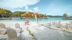 Decoración para una boda en la playa con un altar de arena blanca, cortinas rosas y sillas blancas.