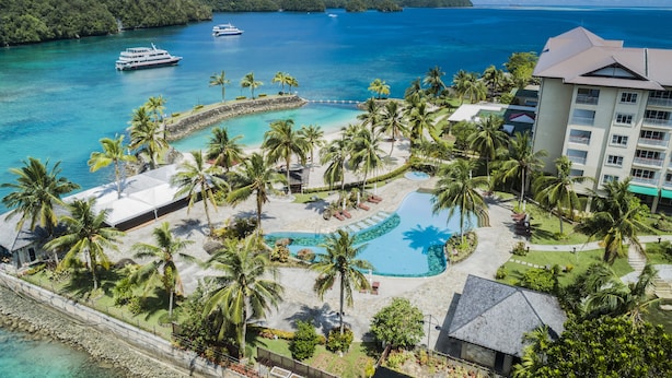 Un resort con piscina, palmeras y vista al océano.