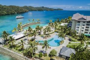 Un complexe hôtelier doté d’une piscine, de palmiers et offrant une vue sur l’océan.