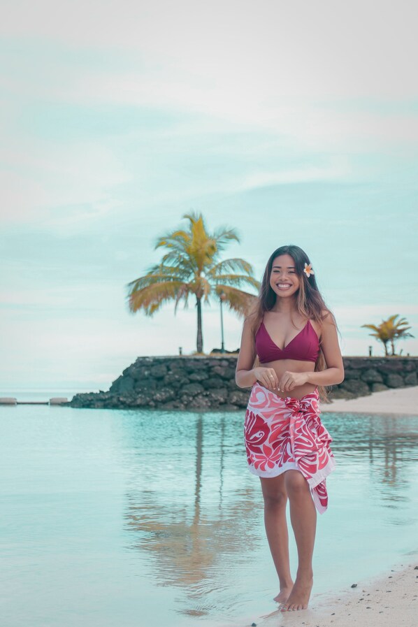 A person standing on a beach with palm trees and a rocky outcrop in the background. - Palau Royal Resort (Malakal Island)