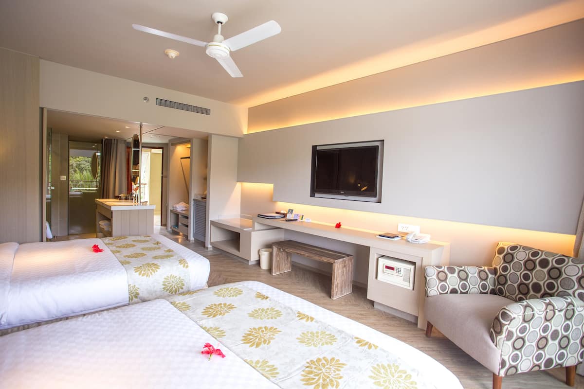 Une chambre d’hôtel avec deux lits, un bureau, une chaise, une télévision et une salle de bain visible à travers une porte ouverte.