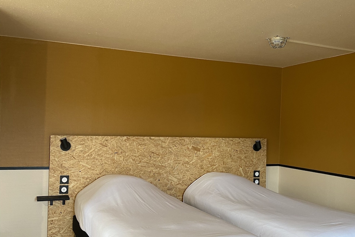 Una habitación con dos camas individuales, un cabecero de madera y una pared de color claro.