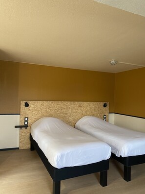 Una habitación con dos camas individuales, un cabecero de madera y una pared de color claro.
