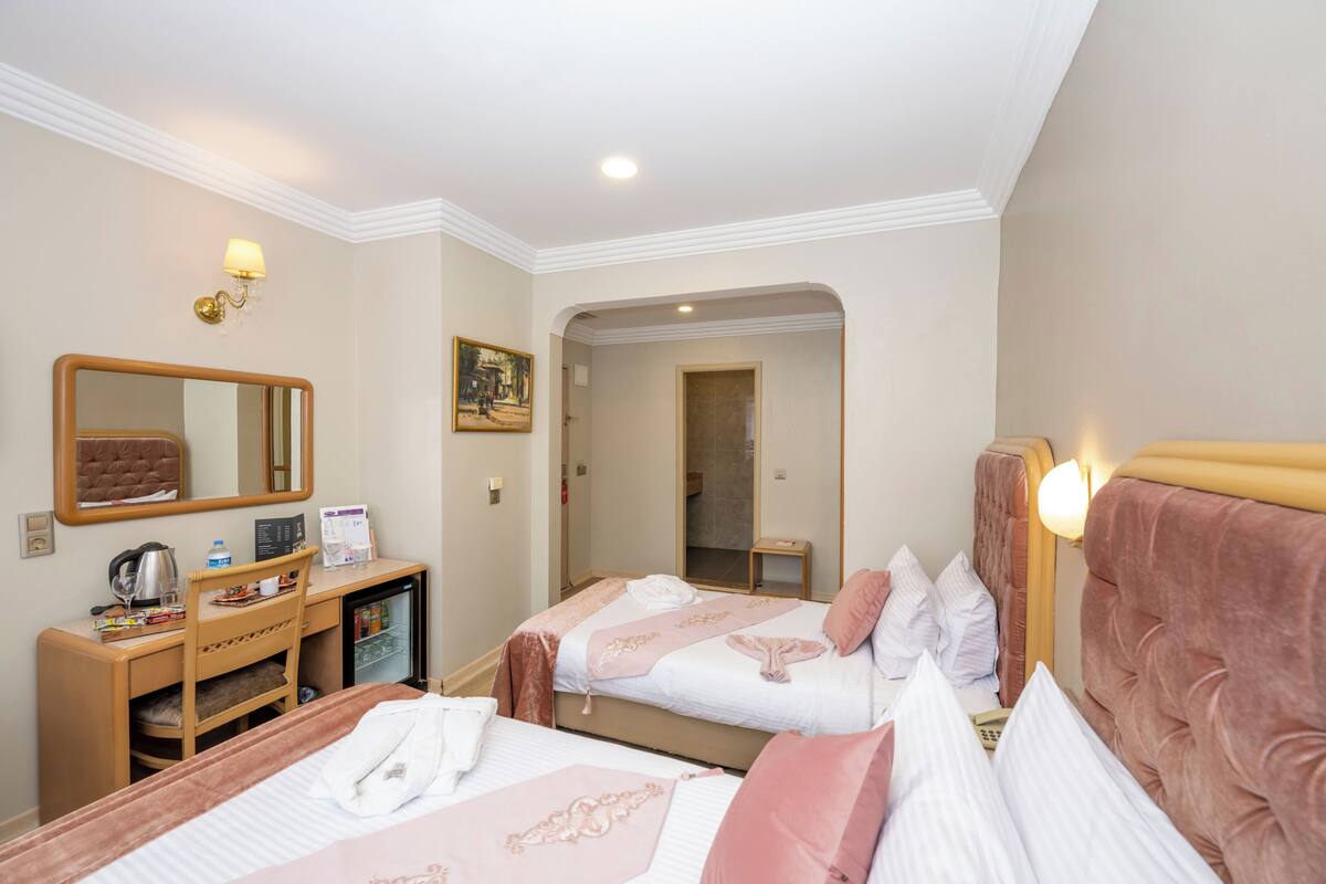 Quarto de hotel com duas camas, uma escrivaninha com computador, espelho e uma pequena cozinha.