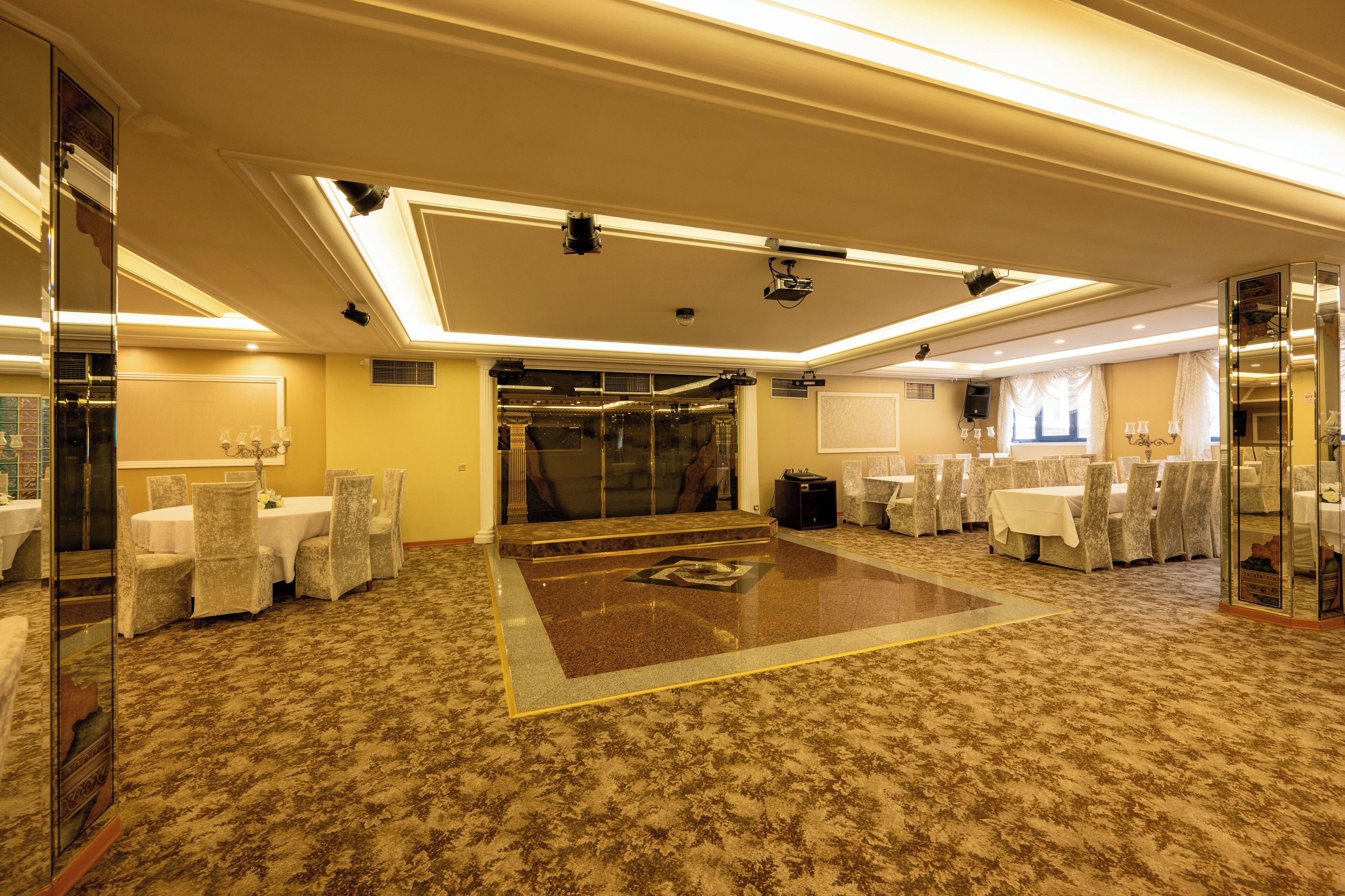 A hotel lobby with a central carpeted area, a reception desk, and a seating area with chairs and tables.