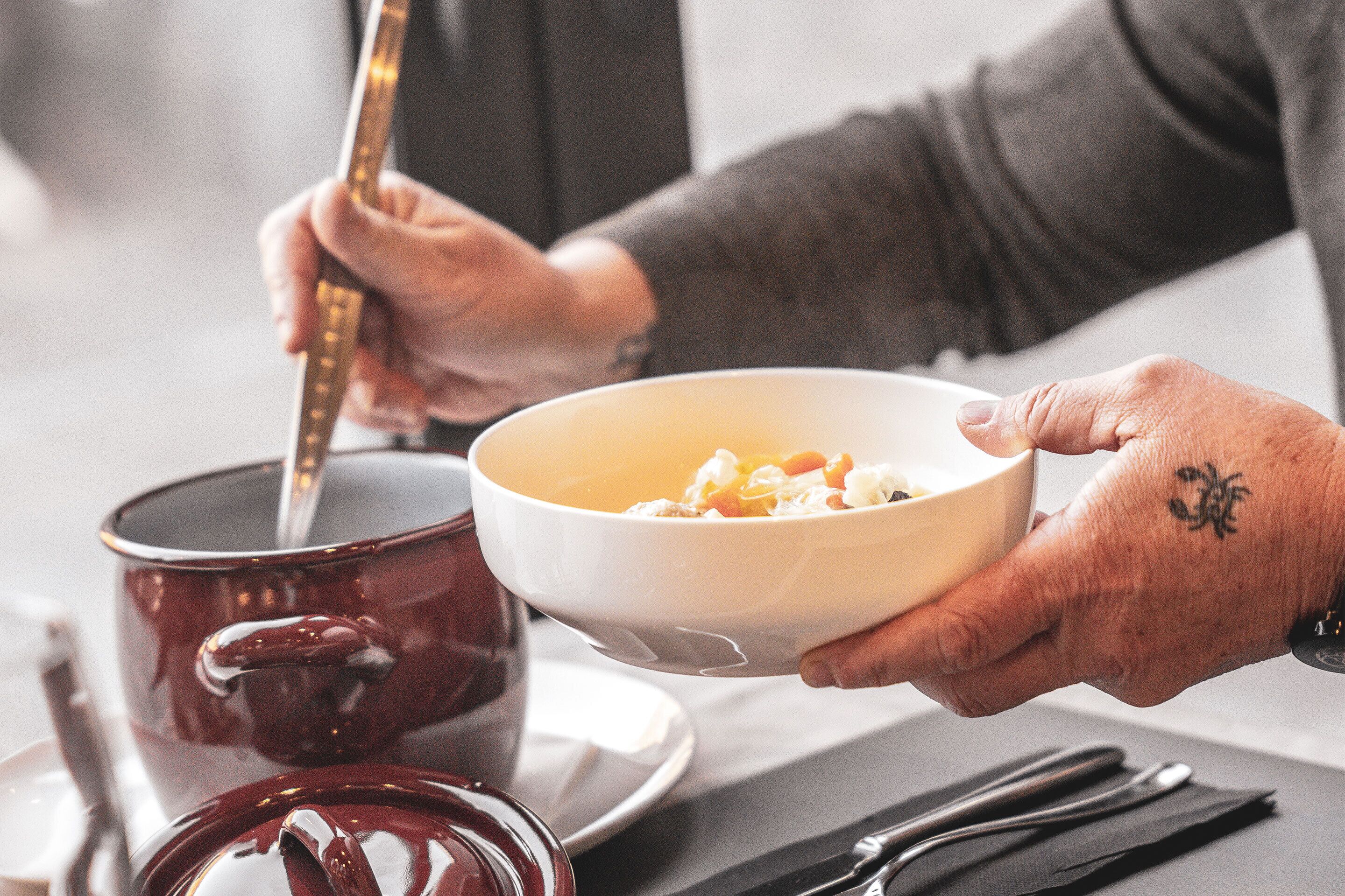 Una persona sosteniendo un plato de comida, con una olla roja y utensilios sobre la mesa.