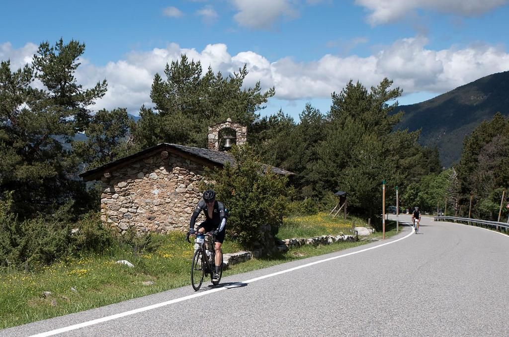 A cyclist on a paved road with a stone building and a bell tower in the background.