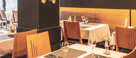 Un restaurante con sillas y mesas de madera, cada conjunto con una copa de vino, cubiertos y una servilleta.