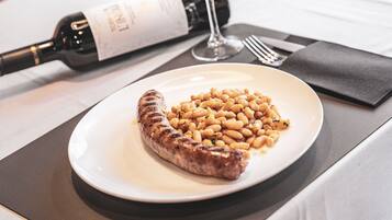 Une assiette avec une saucisse grillée et des haricots, une bouteille de vin et un verre de vin sur une table.