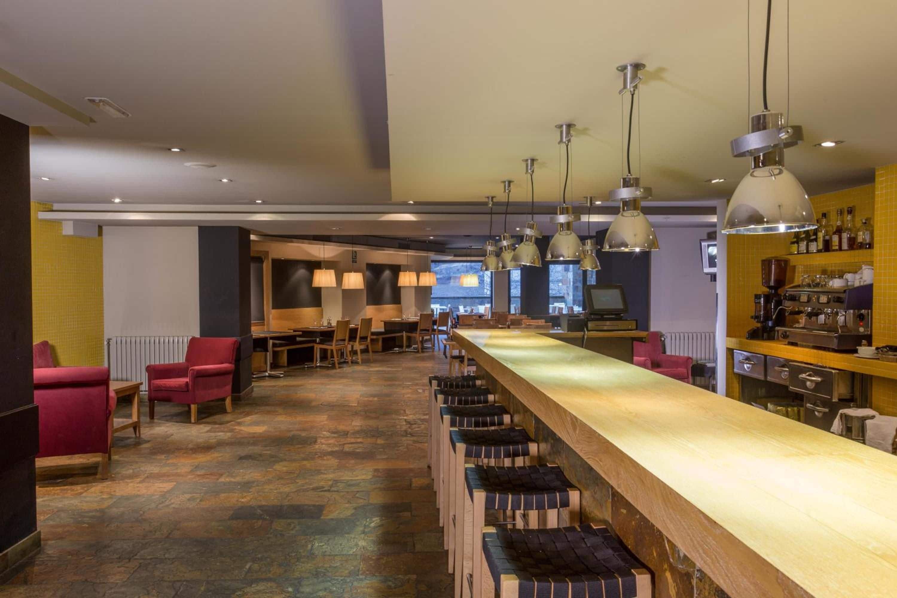 Un área de bar con varias opciones de asientos, incluyendo taburetes y sillas, y una barra alargada.