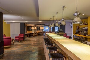 Un área de bar con varias opciones de asientos, incluyendo taburetes y sillas, y una barra alargada.