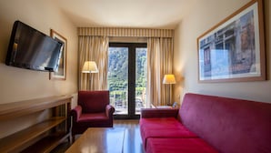 A hotel room with a red sofa, a wooden coffee table, a TV mounted on the wall, and a window with curtains. - Apartaments Shusski by Nexta. (Encamp)