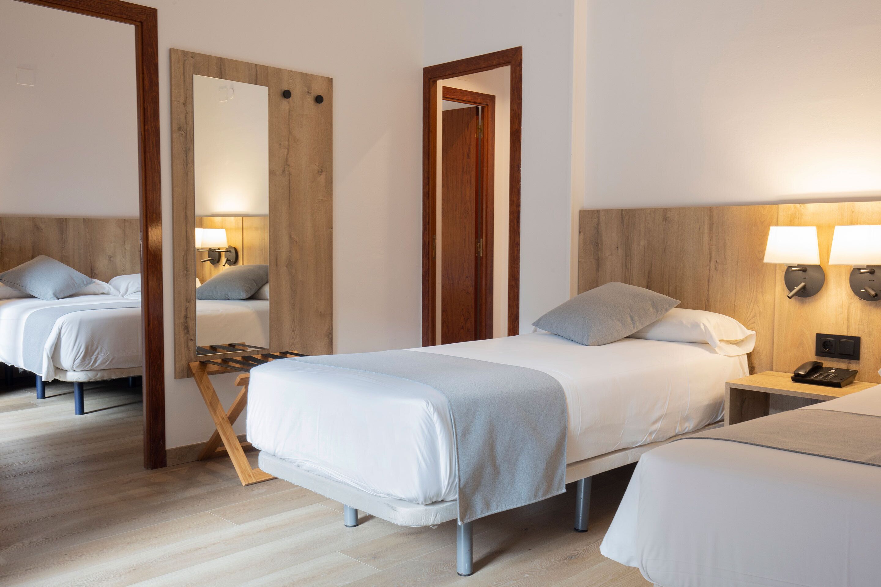 Una habitación de hotel con cama, mesitas de noche, un espejo y una lámpara de pared.