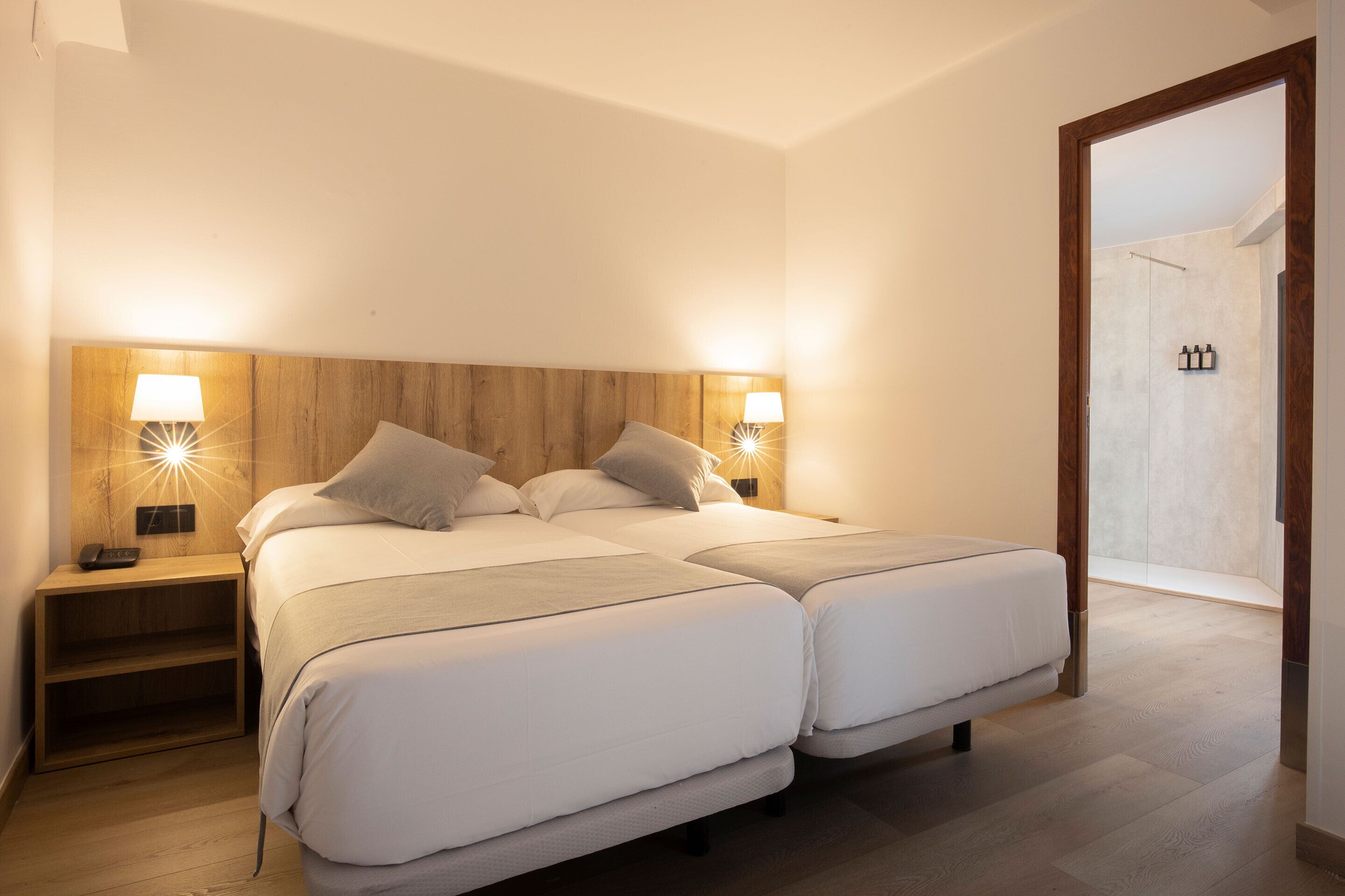 A double bed with two bedside tables, each with a lamp, in a room with wooden flooring and a wooden headboard.