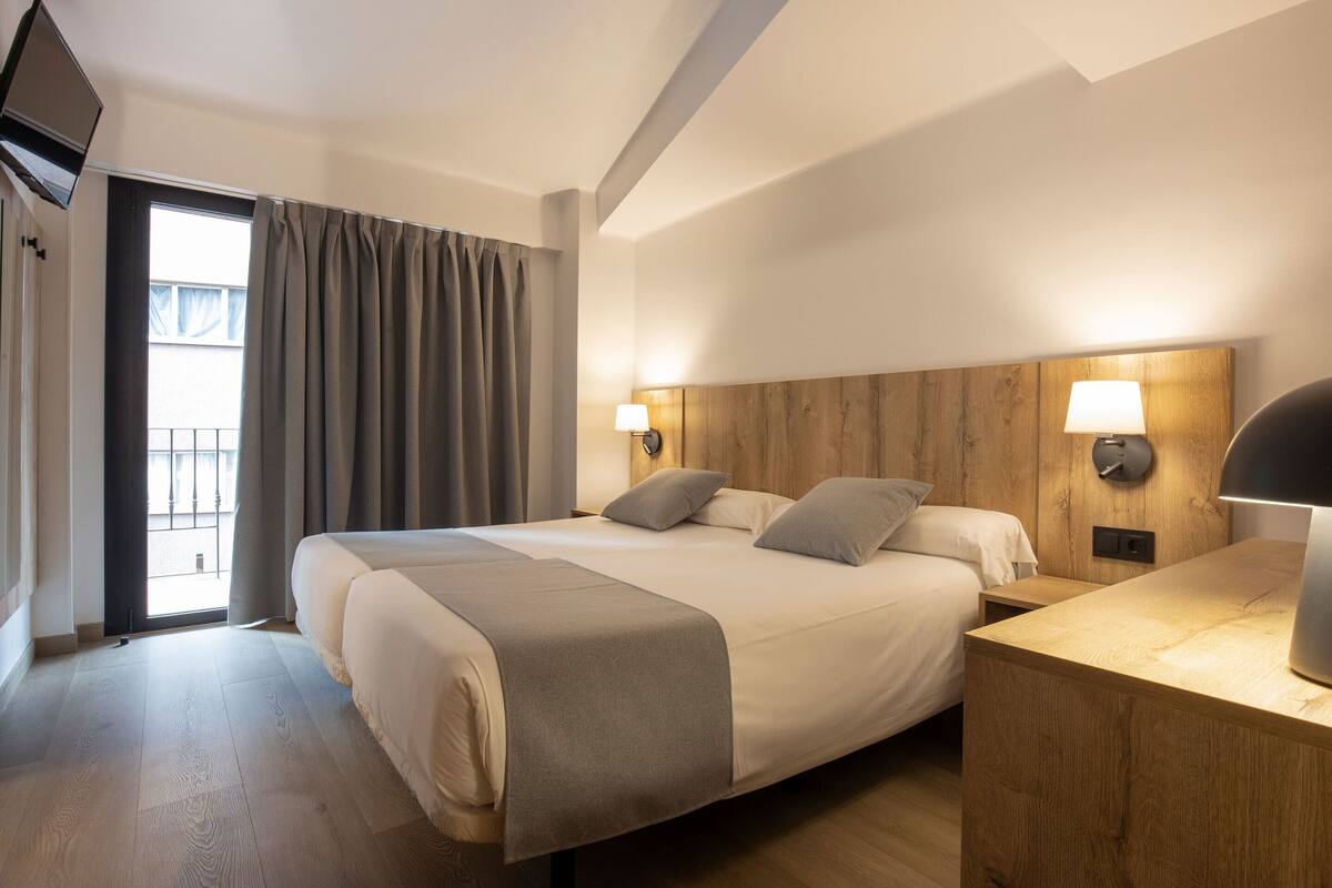 A hotel room with a large bed, bedside lamps, a wooden headboard, and a view of the outside.