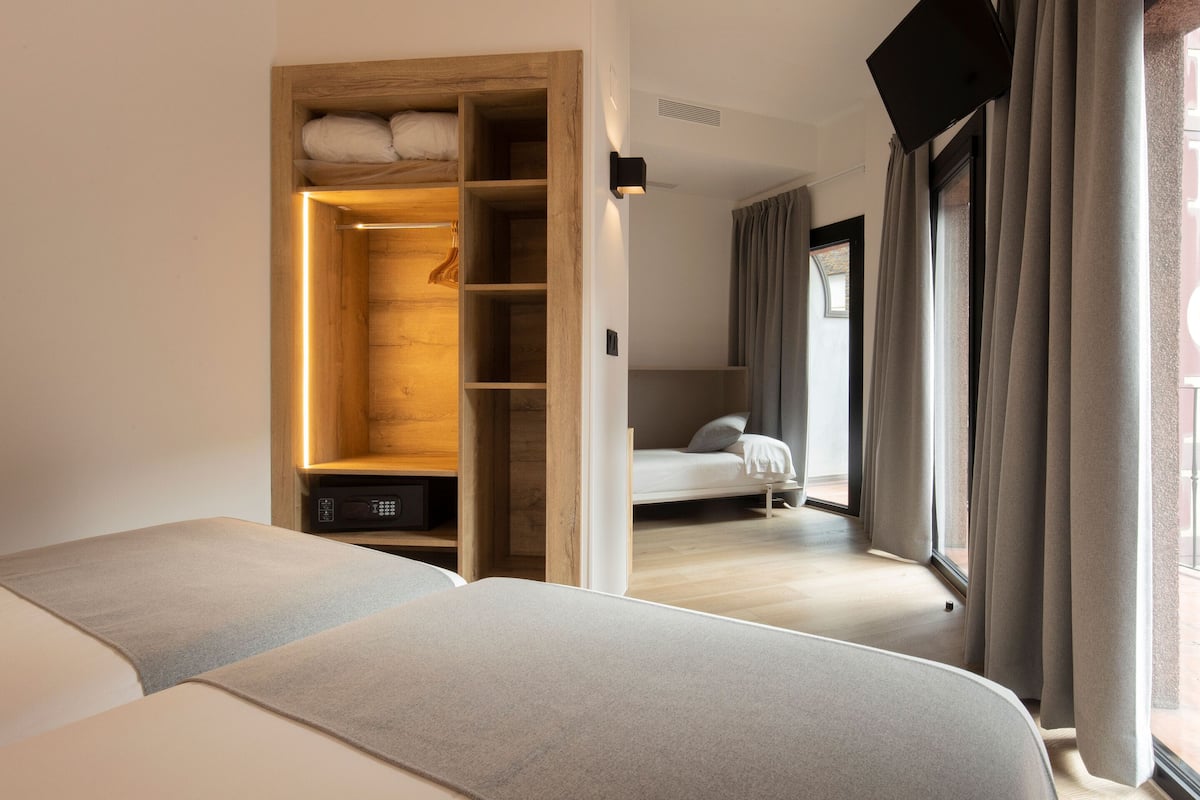 A bedroom with a wooden wardrobe, a bed, and a view through an open door.