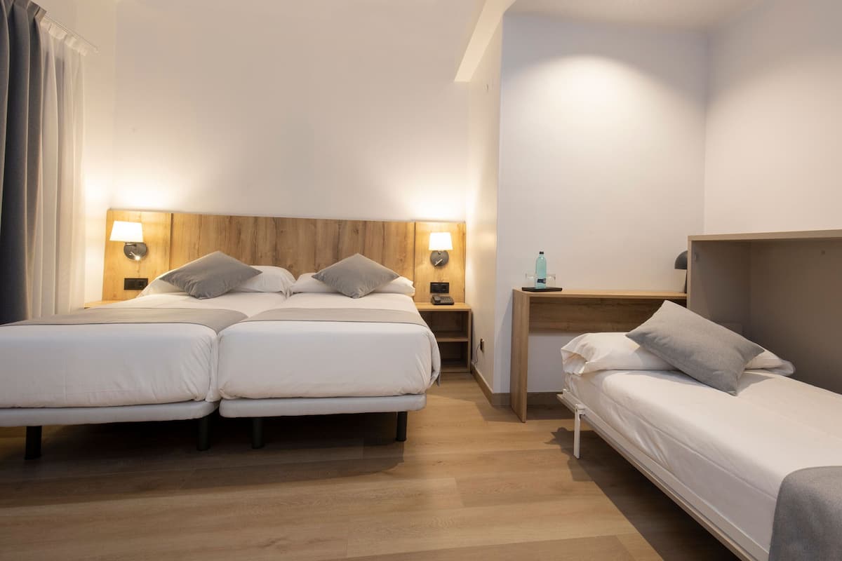 A hotel room with two beds, a wooden headboard, bedside lamps, a nightstand, and a small wooden table.