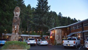 A rustic lodge with a large wooden statue, a stone building, and several parked cars. - Sitzmark Chalet Inn (Ruidoso)