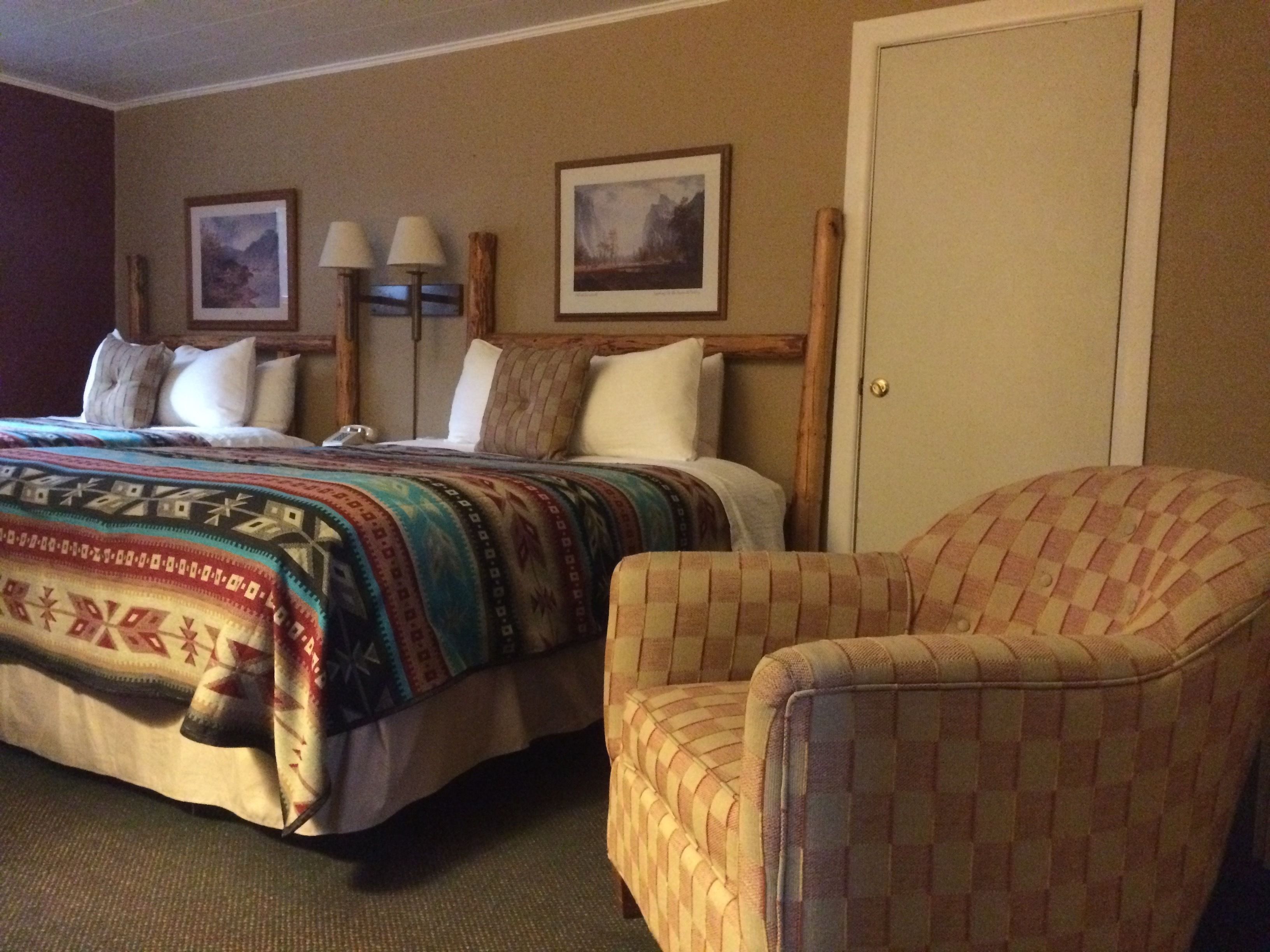 A hotel room with a bed, two pillows, a chair, and two wall-mounted lamps.