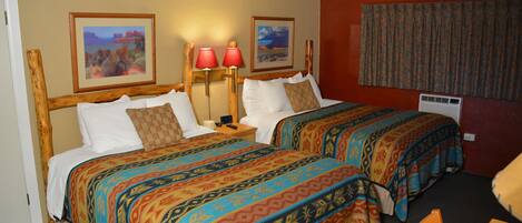 A hotel room with two beds, each with a colorful bedspread, a nightstand with a lamp, and two framed pictures on the wall.