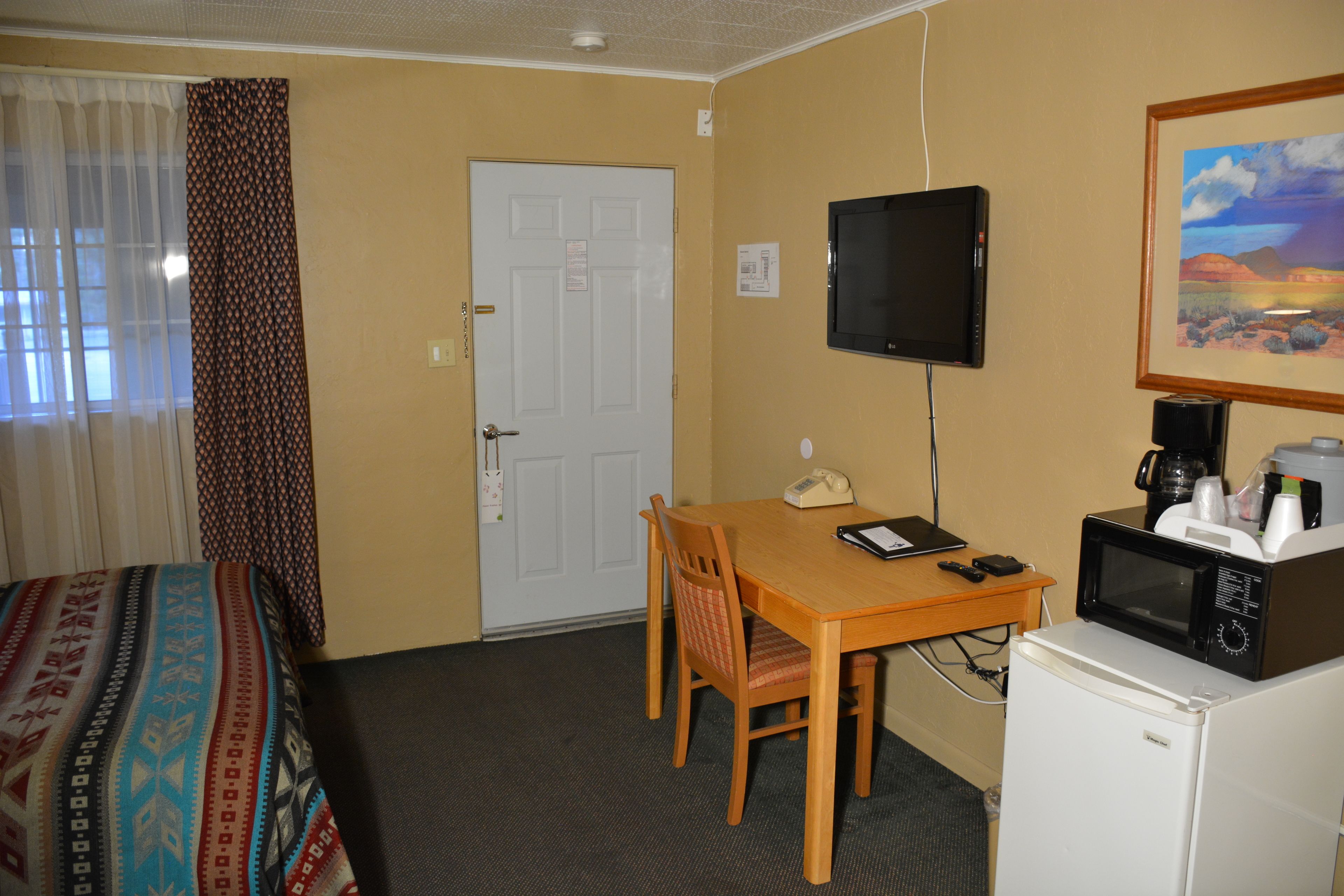 A hotel room with a bed, a desk with a computer, a microwave, and a television.
