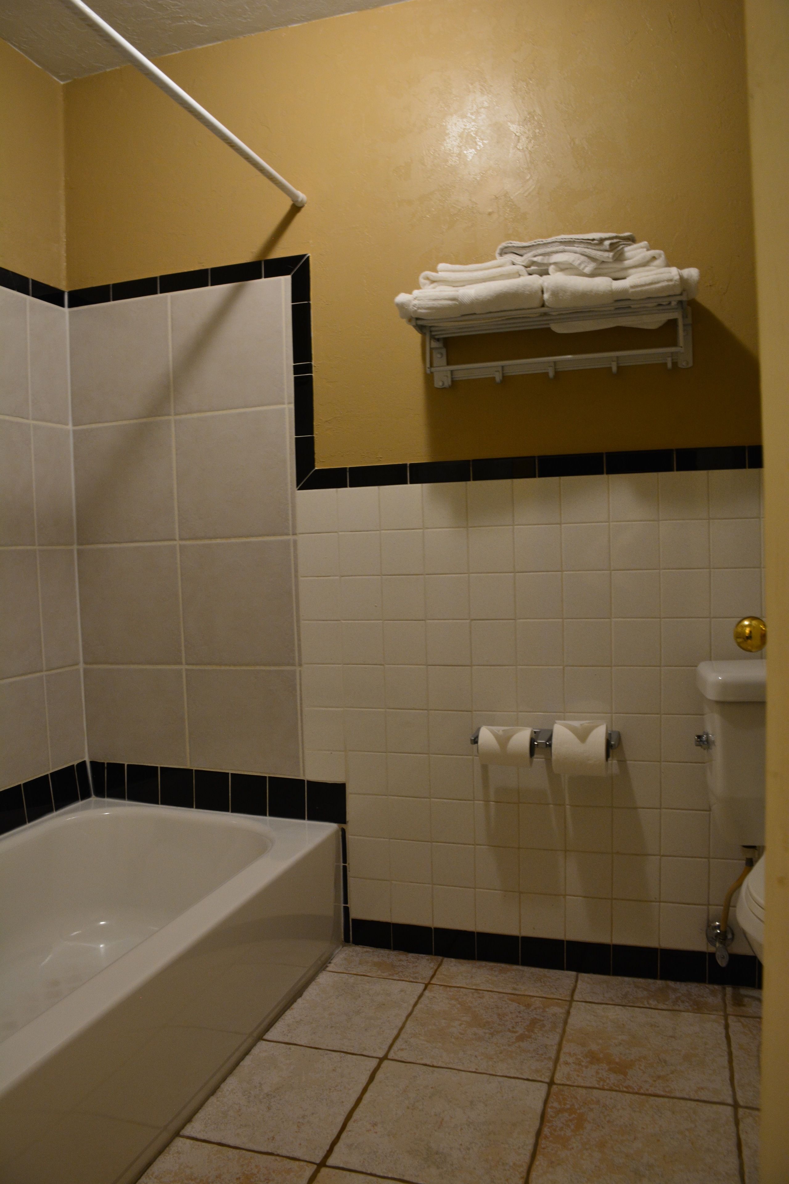 A bathroom with a bathtub, white tiles, a towel rack with folded towels, and a toilet.