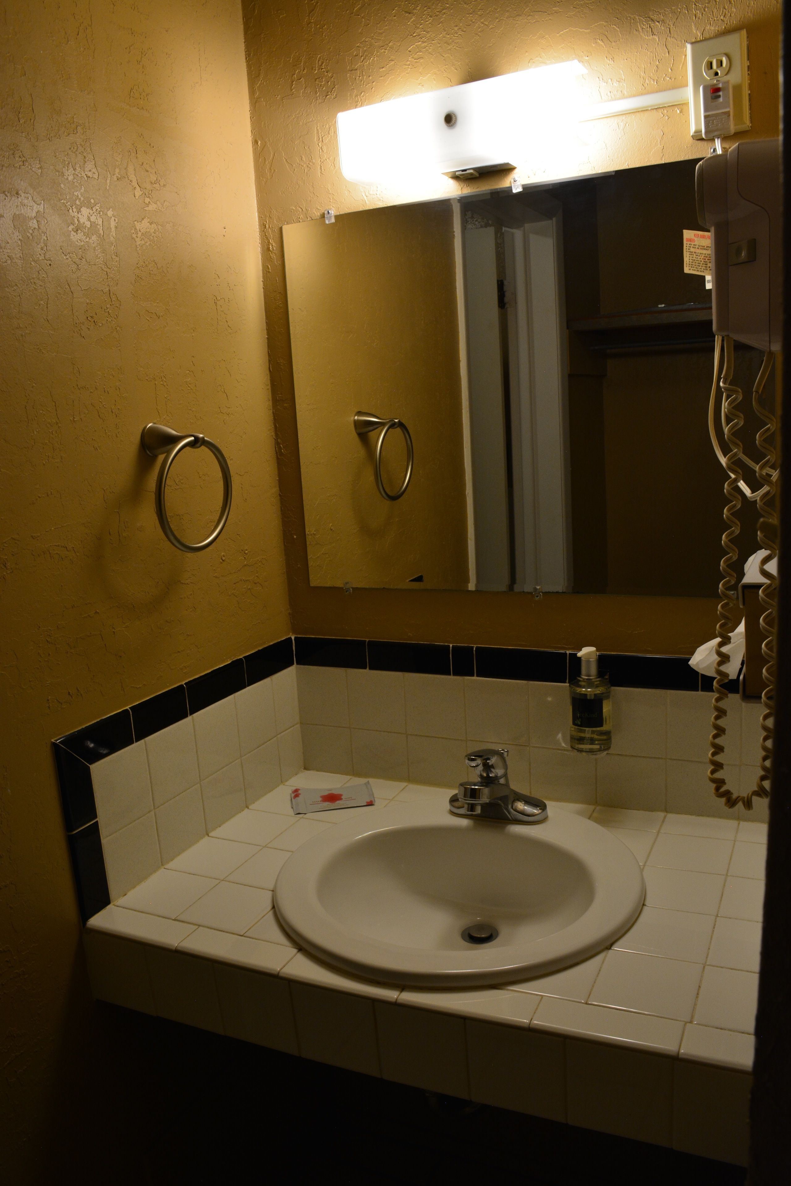 A bathroom with a sink, mirror, towel ring, and a hand dryer.