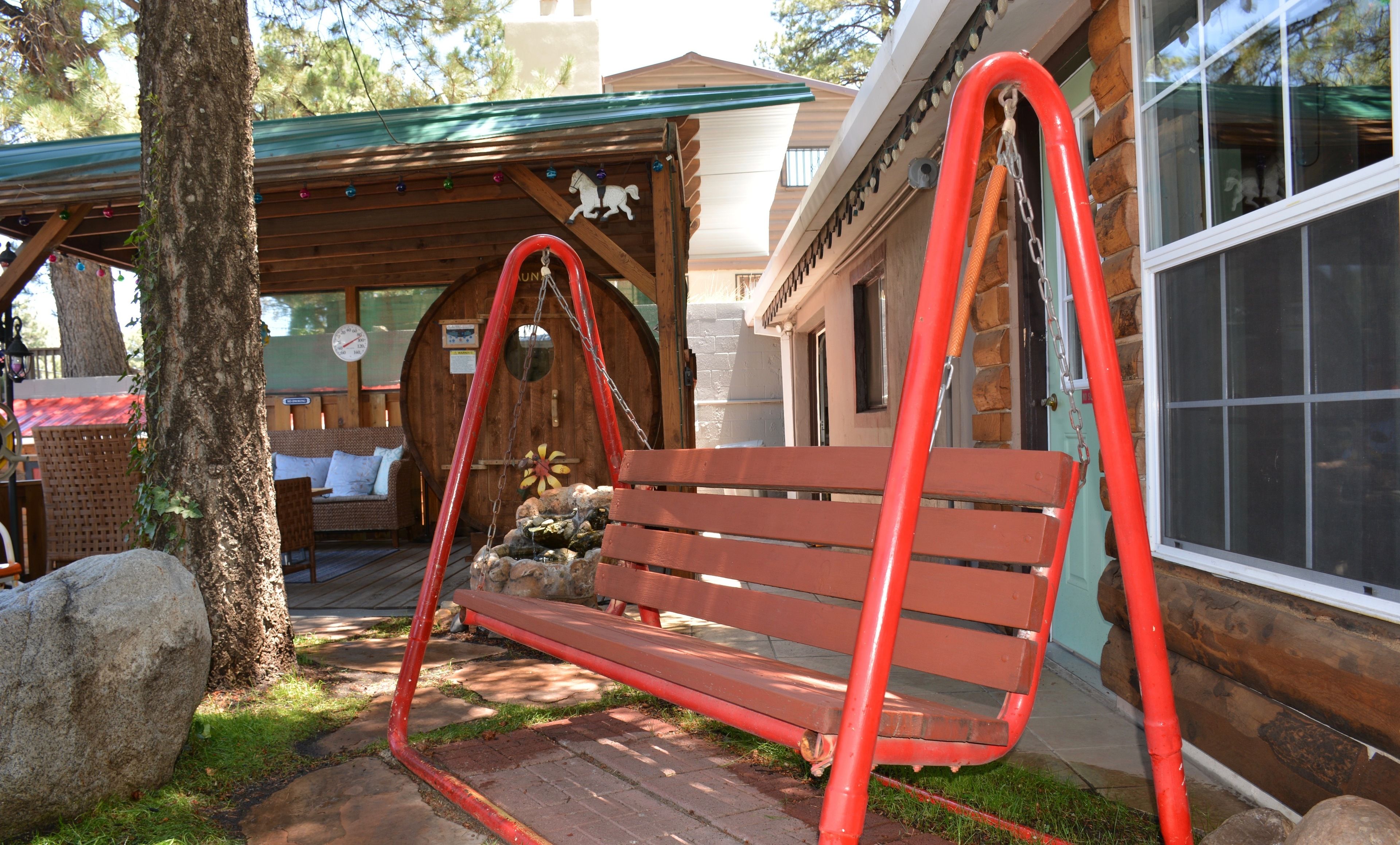 A wooden swing bench with metal chains, set on a stone pathway, surrounded by a wooden deck and a stone wall.