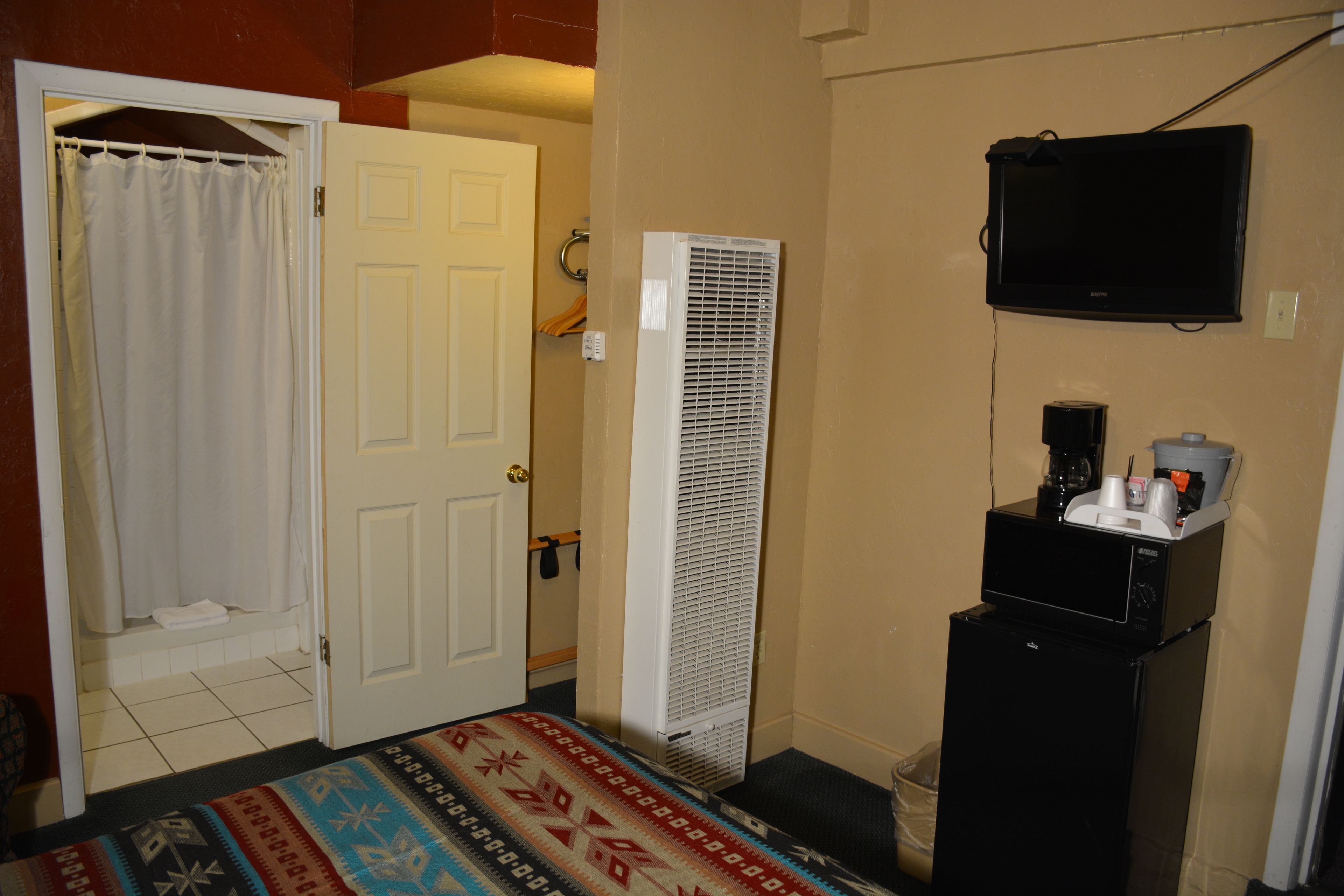 Une chambre d’hôtel avec un lit, une porte blanche, un climatiseur blanc, un téléviseur noir et un petit réfrigérateur.