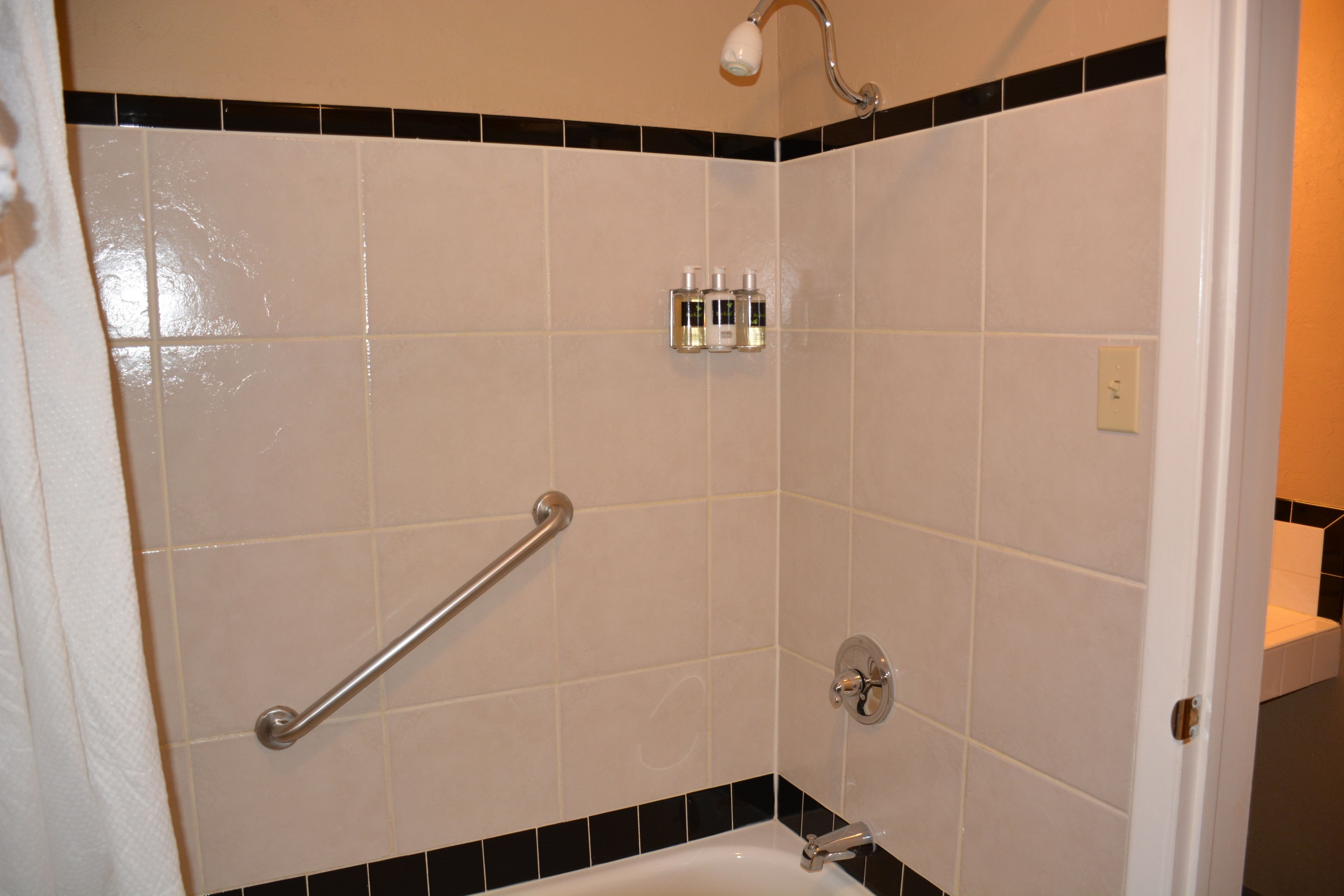 A bathroom with white tiles, a shower, a grab bar, and a towel rack.