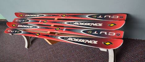 A set of four red and black Rossignol skis on a wooden stand against a grey wall.