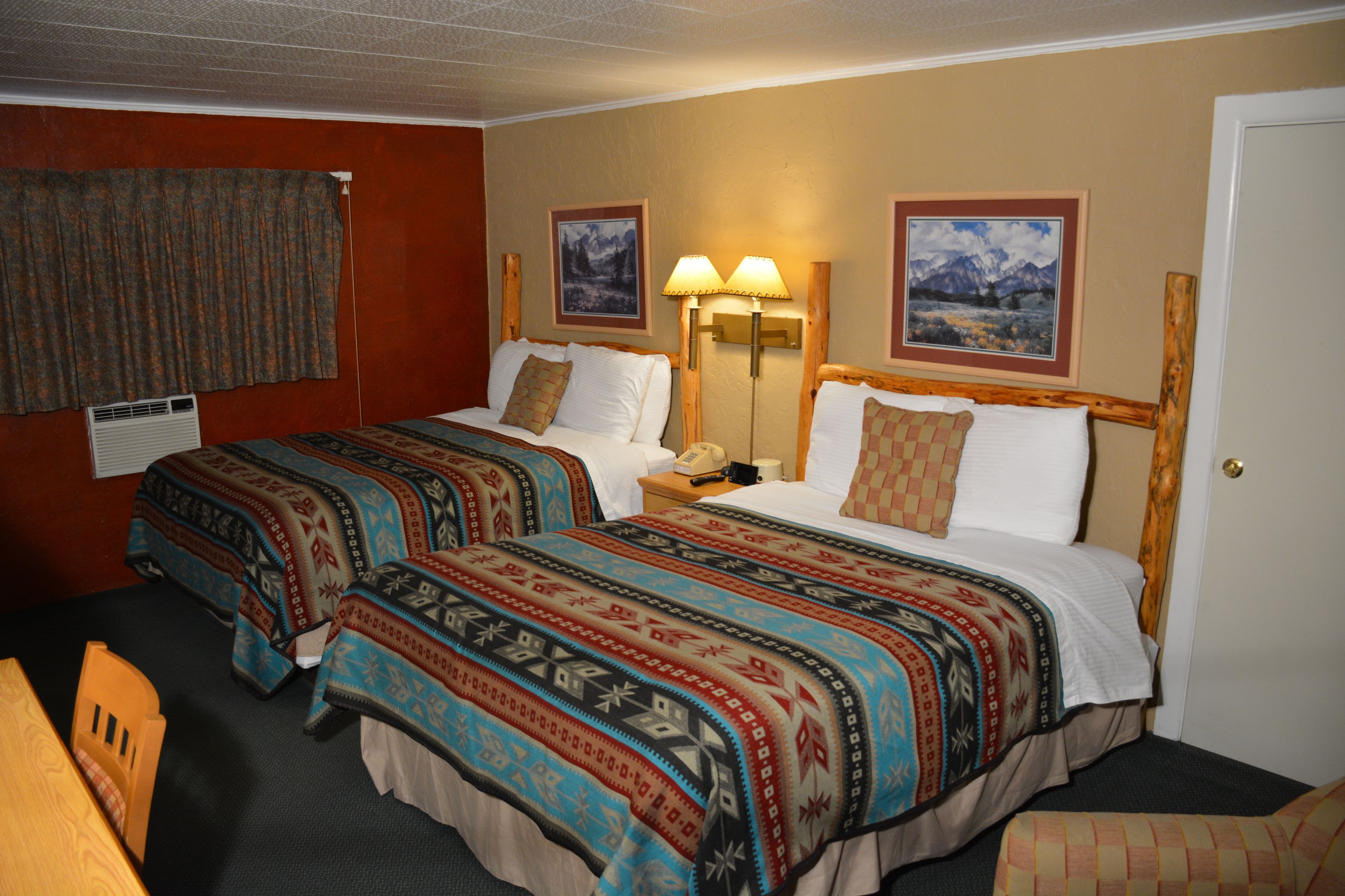 A hotel room with two beds, a nightstand, a lamp, and a door.