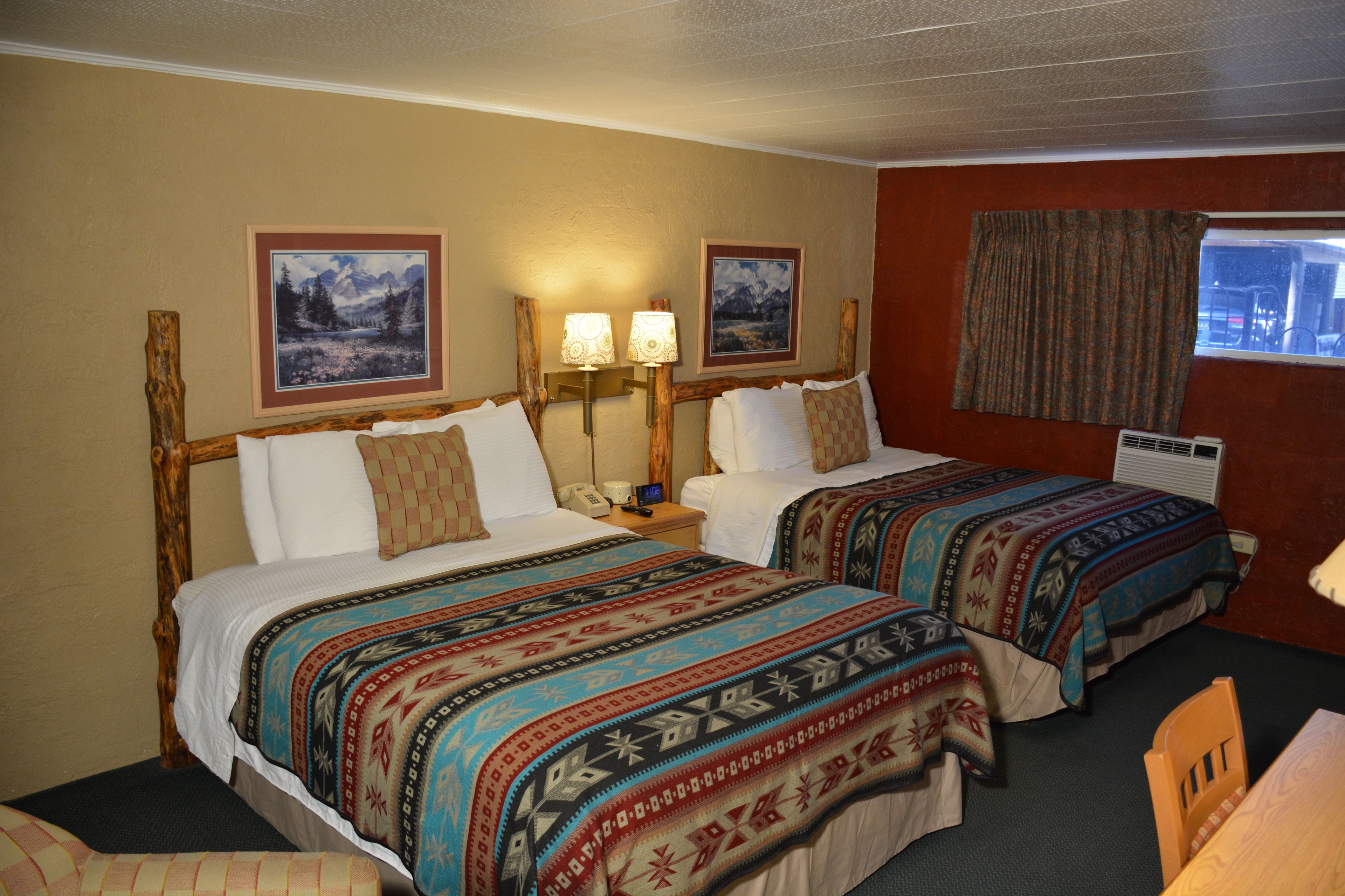 Una habitación de hotel con dos camas, cada una con ropa de cama estampada, cabeceros de madera, lámparas de noche y cuadros en la pared.