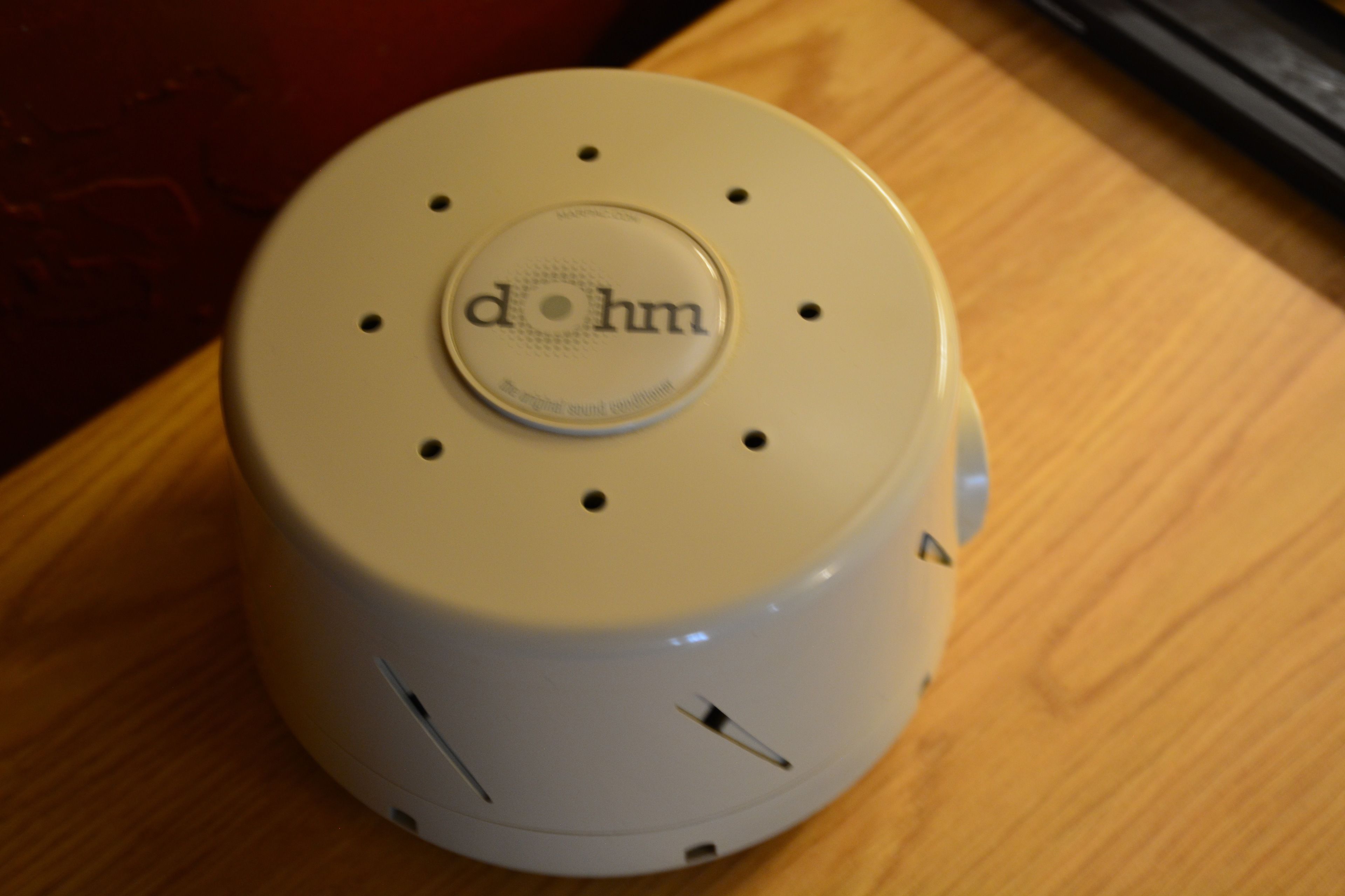 A white device with the text "dohm" on its top, placed on a wooden surface.