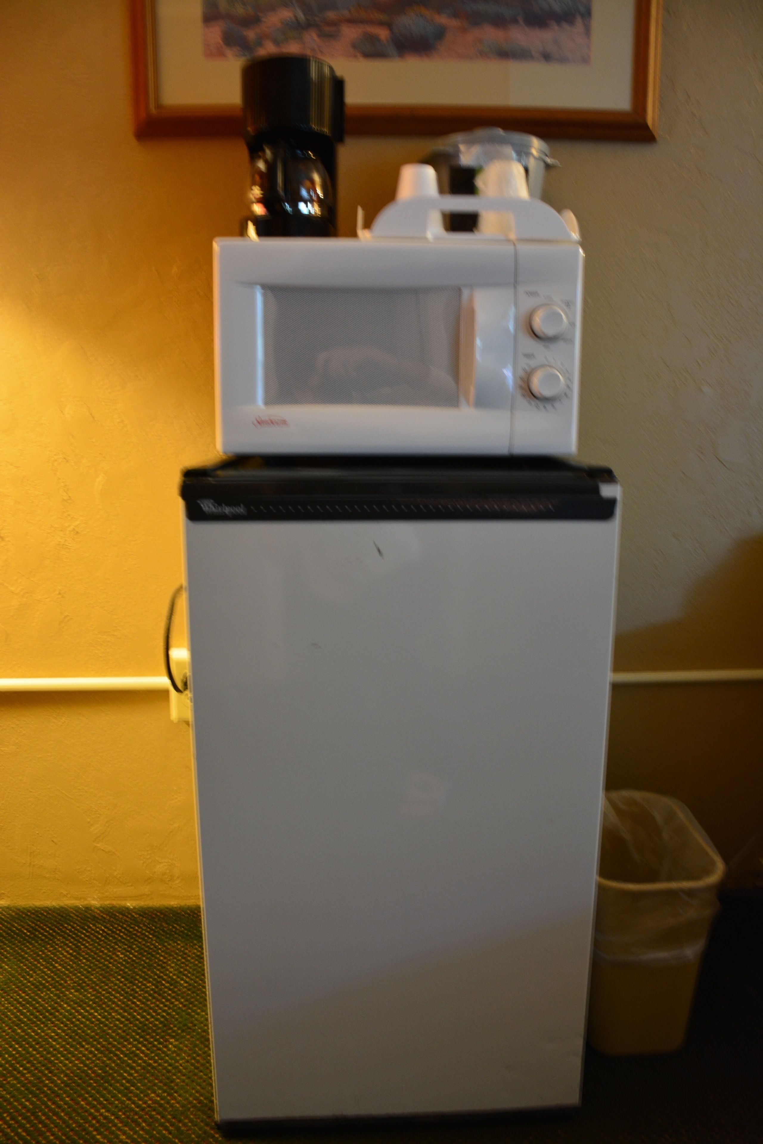 A compact refrigerator with a microwave on top, placed on a green mat against a yellow wall.