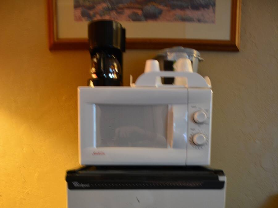 A compact refrigerator with a microwave on top, placed on a green mat against a yellow wall.