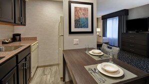 A modern hotel room with a kitchen area, a dining table set with plates and cutlery, a flat-screen TV, and a framed abstract painting on the wall. - Homewood Suites by Hilton Edgewater (Edgewater)