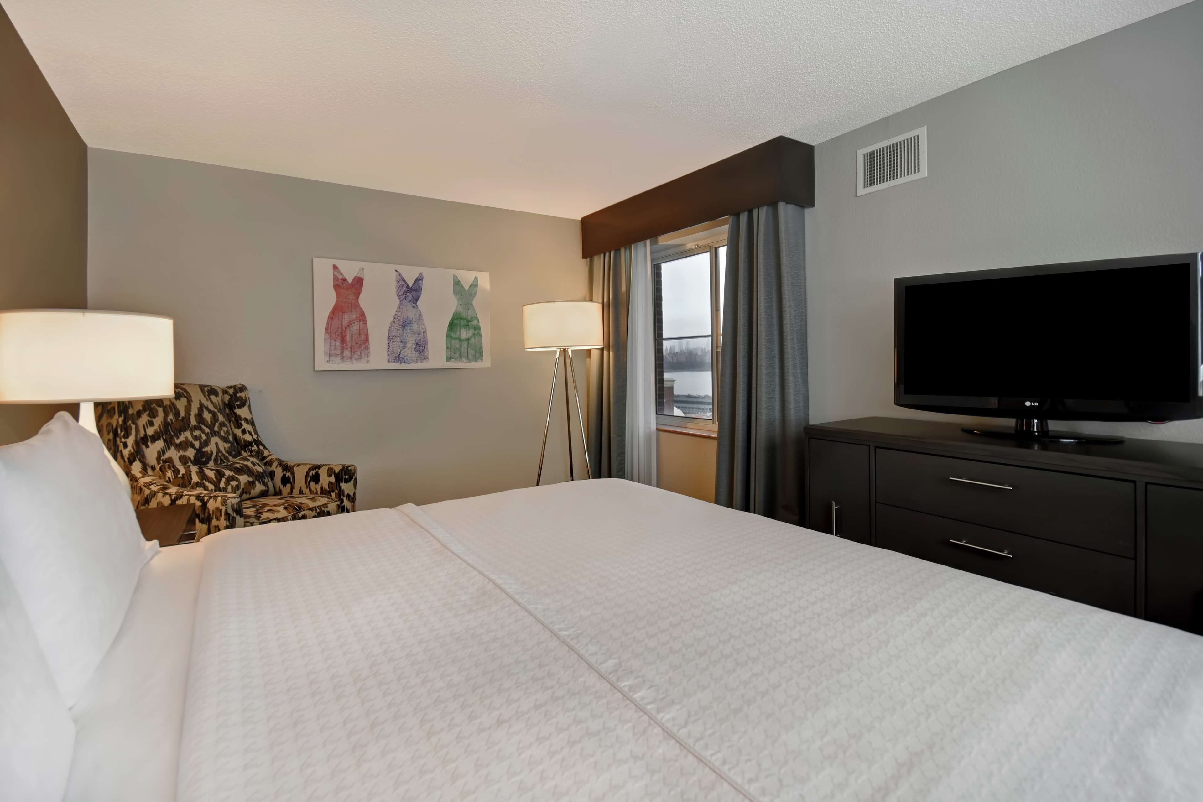 A hotel room with a large bed, a flat-screen TV, a desk with a lamp, and a chair.